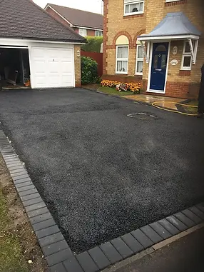 Freshly paved asphalt driveway leading to a brick house