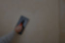 A hand holds a black and red grout float, smoothing tile grout on light beige wall tiles.