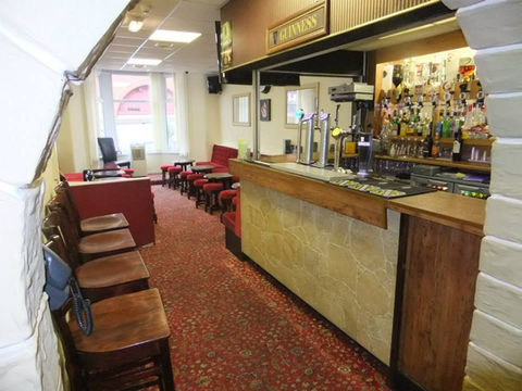 Cozy pub interior with a wooden bar on the right and red cushioned seating on the left