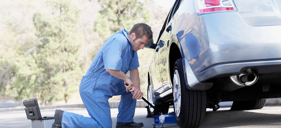 A mechanic kneels beside a car, using a jack to lift the vehicle