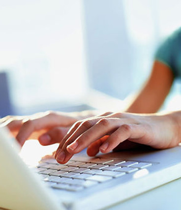 Hands typing on a laptop keyboard in a bright, sunlit room
