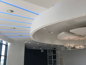 An interior room with curved white ceiling panels highlighted by blue strip lighting