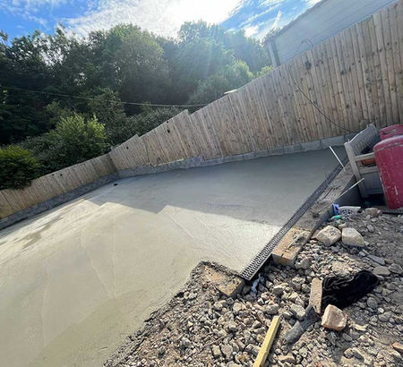 Freshly poured concrete pad in a backyard, bordered by a wooden fence