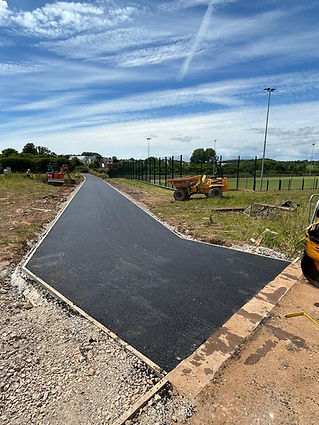 Freshly paved narrow road veers right, bordered by grass and construction machinery