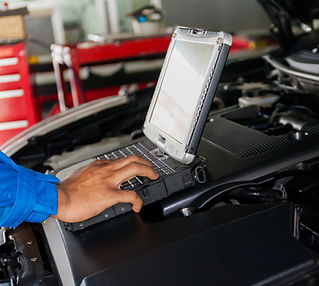 A mechanic uses a laptop on a car engine