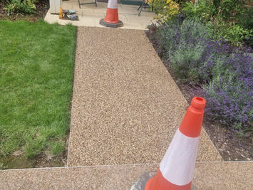 A straight resin-bound gravel garden path leading towards a blue metal container behind construction fencing