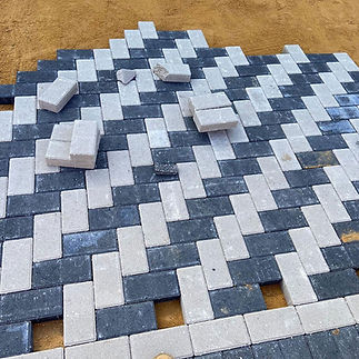 Herringbone pattern of gray and charcoal paving stones on sand