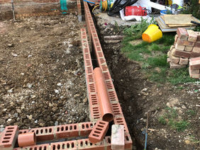 Close-up view of the newly laid red brick cavity wall foundations with an open drainage trench running alongside