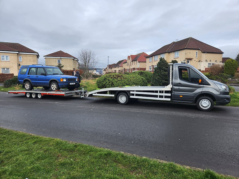 A blue SUV is being towed by a flatbed truck on a residential street