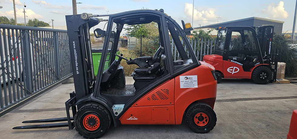 Red forklift parked outdoors on concrete with greenery and fencing