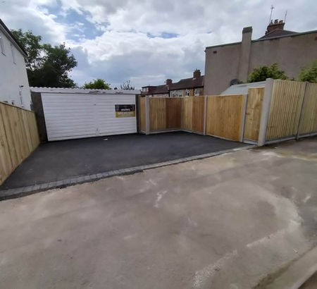 A newly paved driveway leads to a white garage with a wooden fence