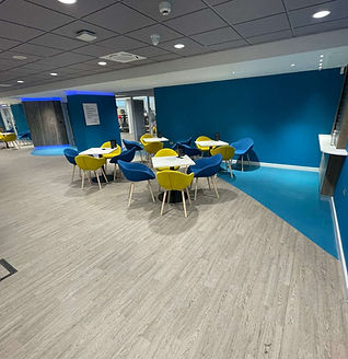 A modern lounge area with blue and yellow chairs around small white tables