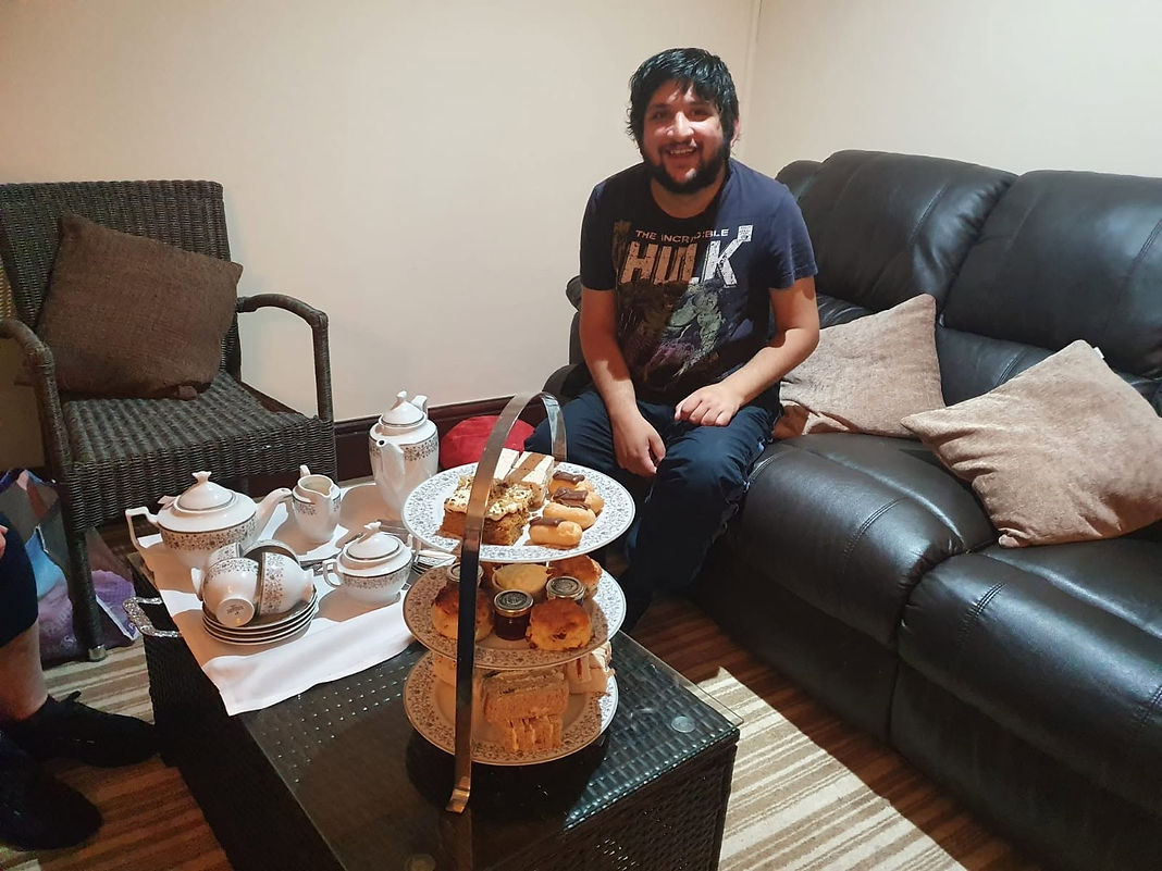 A man sits on a couch, enjoying a tray filled with tea and assorted cakes