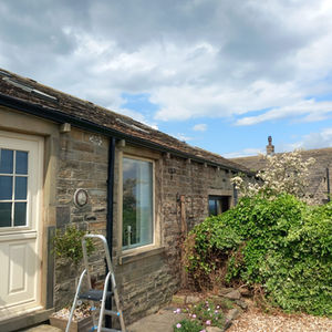 Stone cottage with a white door, surrounded by lush greenery and blooming bushes