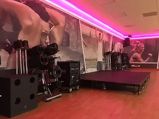 Fitness studio with wooden floors, pink neon lighting, and a stage