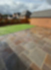 Wet patio with stone tiles beside a green artificial lawn