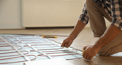 A person in a plaid shirt installs underfloor heating on a wooden floor