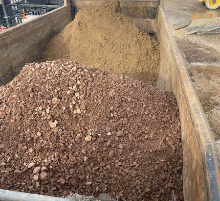 A truck bed loaded with piles of sand and reddish-brown gravel on a construction site