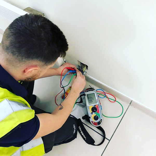 A person in a high-visibility vest repairs an electrical outlet, holding colorful wires