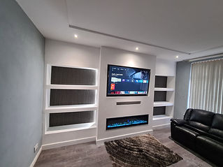 A contemporary living room feature wall showcases a recessed television displaying a streaming menu above a sleek electric fireplace with blue flames