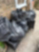 Black garbage bags piled on a wicker outdoor chair against a brick wall