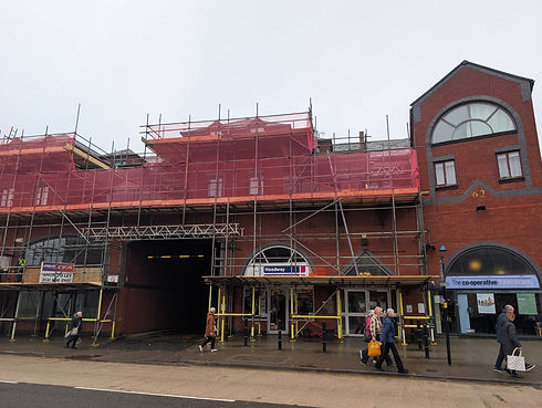 Red scaffolding covers a brick building with arched windows and shops below