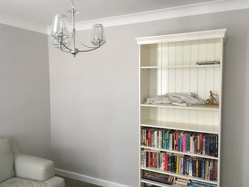 A cozy room with light gray walls. On the right, a white bookshelf holds colorful books,