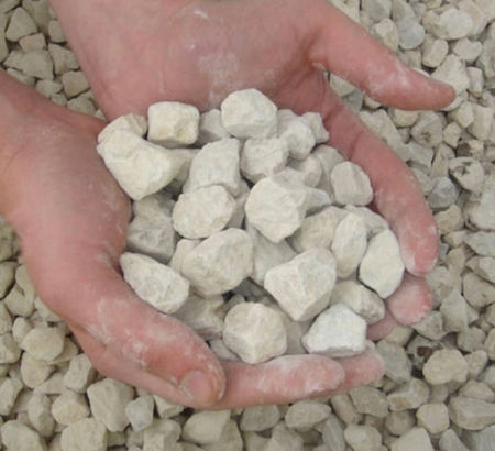 Hands holding a pile of light-colored, rough, small stones over a larger pile of similar stones