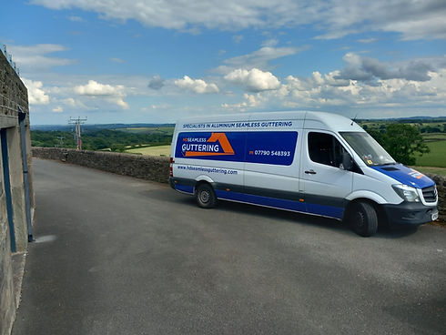 A white van labeled "Seamless Guttering" is parked on a rural road