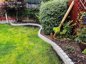 A curved garden border featuring a low, grey cobblestone edging stones wall set in concrete