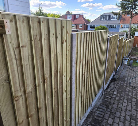 Newly installed wooden fence panels line a paved pathway in a residential area