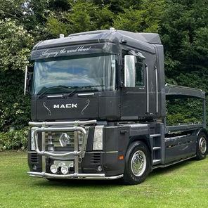 Sleek, black semi-trucks with tall cabins are parked on a lush green lawn