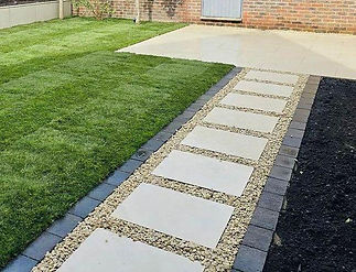 A garden path with rectangular stone slabs bordered by small pebbles leads to a paved patio