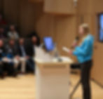 Youth Board member in blue jumper speaking to a theatre of people with a microphone