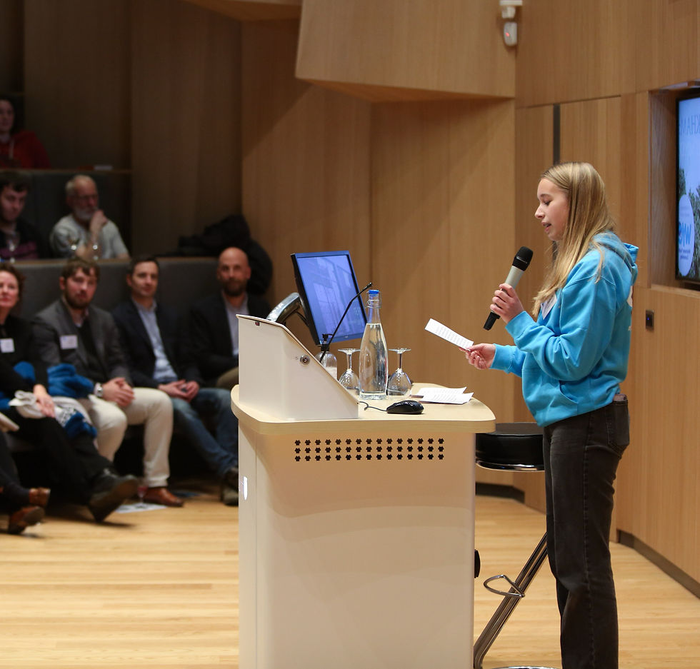 Youth Board member in blue jumper speaking to a theatre of people with a microphone