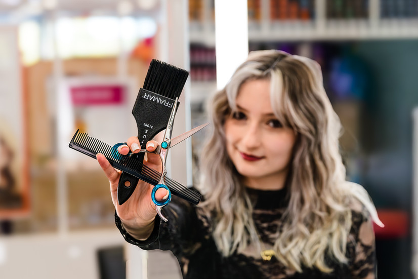 hair stylist holding out comb, scissors, and highlight brush in front of her