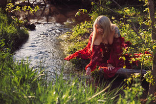 A mother's Dream Maternity Photoshoot of her sitting by a creek playing in the water with her hand