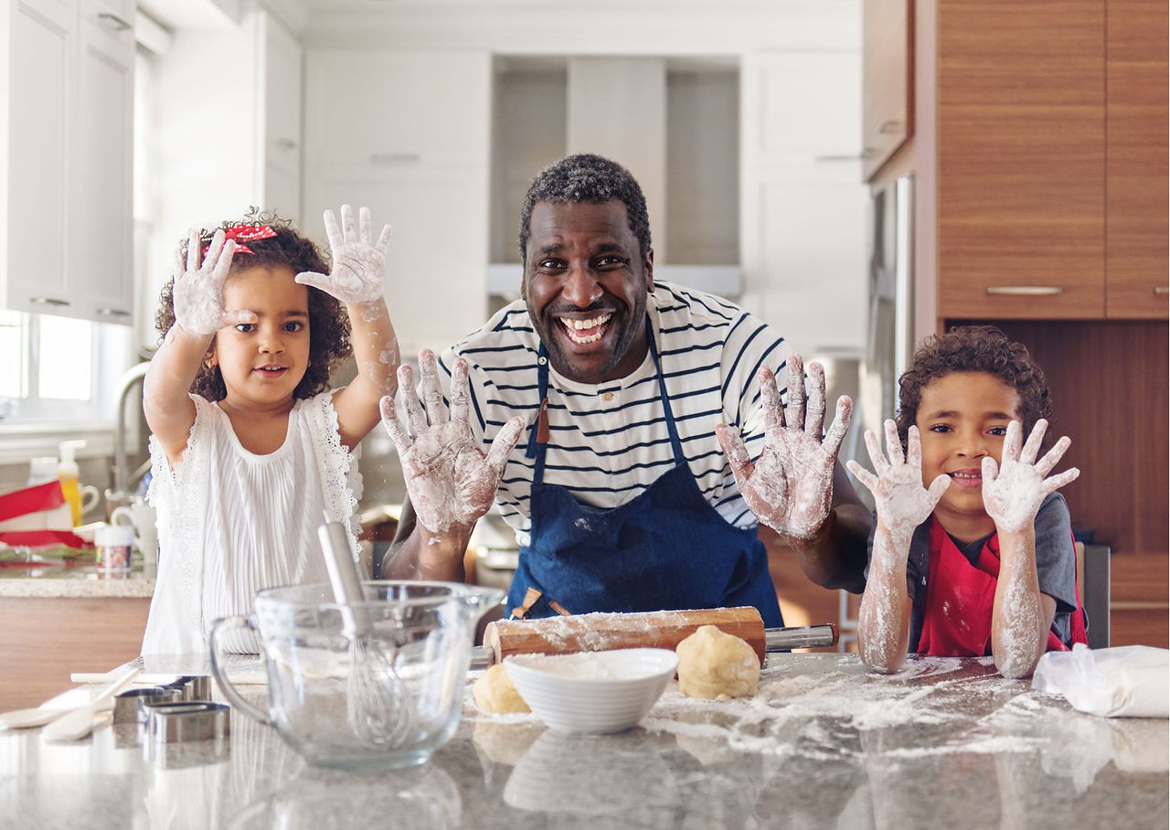 pai com filhas fazendo comida e lanche com maos sujas de farinha de trigo