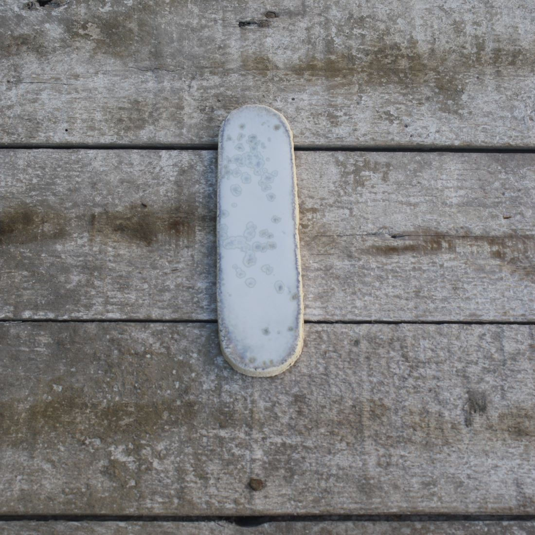 Porte-couteau artisanal en grès blanc émail clair à cristallisations posé sur table en bois vue du dessus