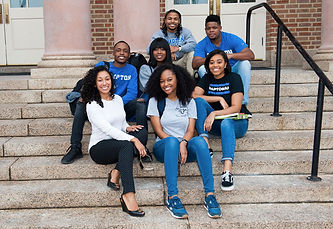 A group of seven college aged students wearing blue and white outfits sitting on steps and smiling.