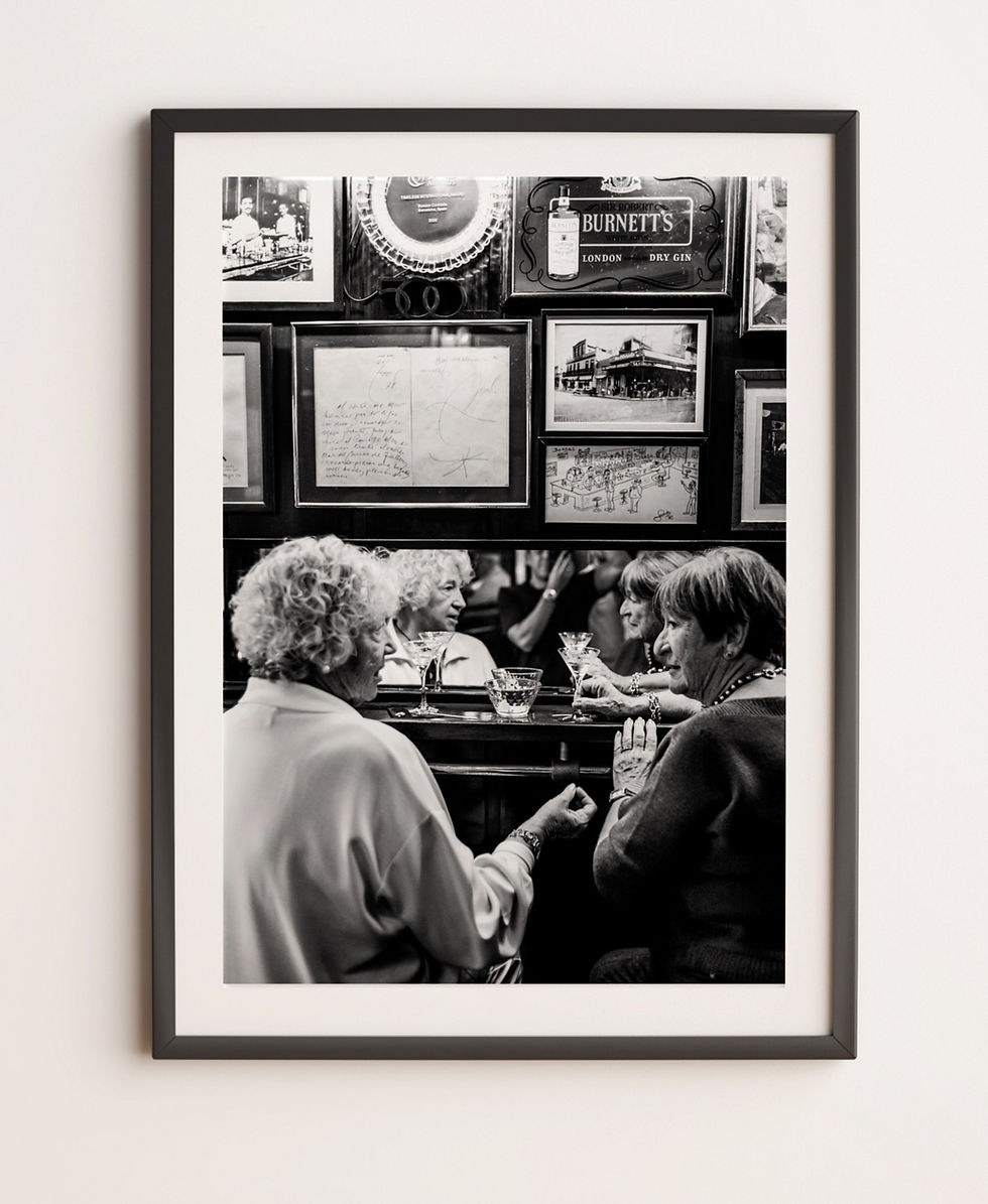 A black-and-white photo of three elderly women sitting at a bar, engaged in conversation. They are reflected in the mirror.