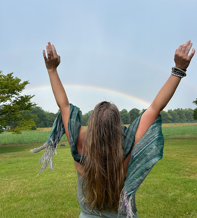 Woman with hands raised high in front of a rainbow stretching across the horizon