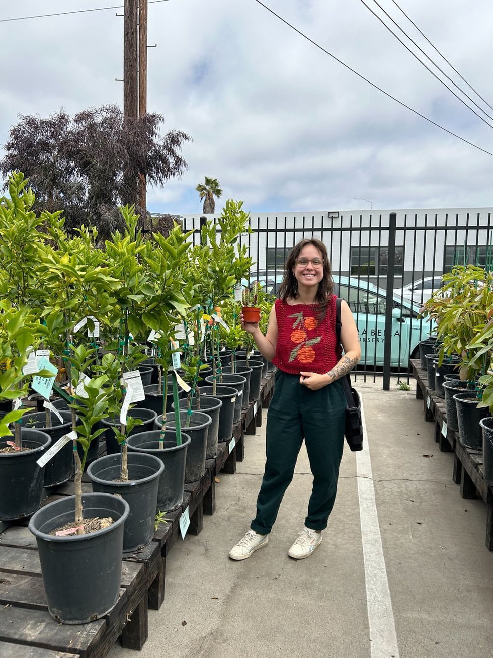 Olivia in orange sweater with orange tree sapling!