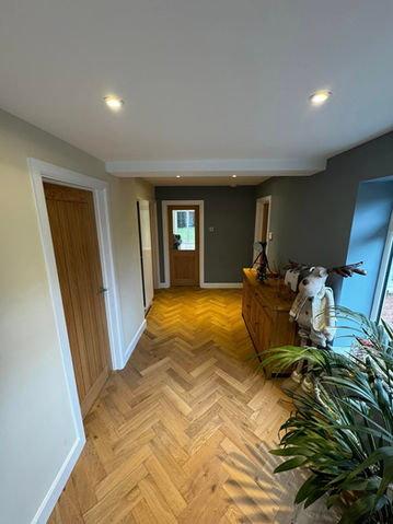 Hallway with herringbone-patterned oak flooring, modern doors, and warm lighting.