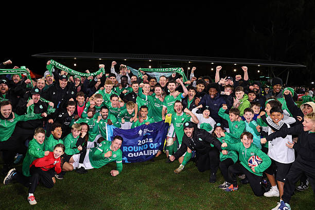 A large group in green soccer attire celebrates on a field, holding a banner reading "2025 Round of 16 Qualifer." Joyful and festive mood.