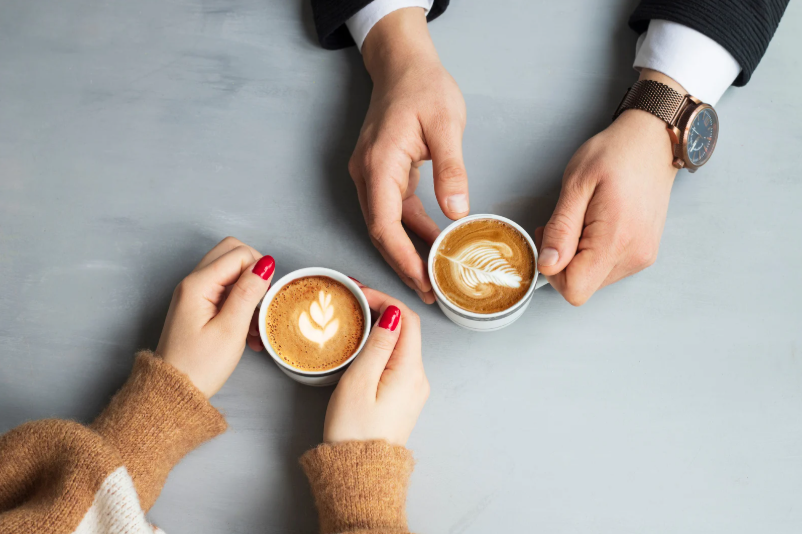 two sets of hands holding coffee on a table