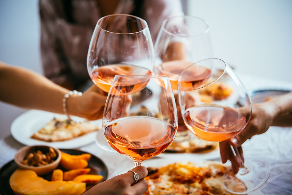 Four people clink glasses of rosé wine over a table with pizza and snacks. Warm, celebratory mood in a cozy setting.