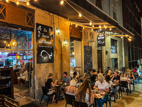 Außenbereich von La Tasca del Barrio in Alicante: kleine Tische in einer belebten Gasse