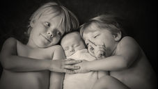 sepia photo of two older kids and a newborn between them, all giggling
