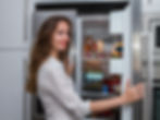 Photo of a woman standing in front of a refrigerator with the door open.